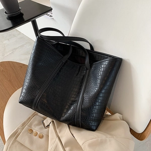 Detail of a large black tote bag with crocodile pattern resting on a white chair