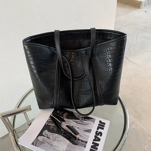 Detailed close-up of a black crocodile pattern tote bag on a modern glass table