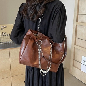 Sac fourre-tout marron en similicuir avec chaîne métallique et perles porté par un mannequin
