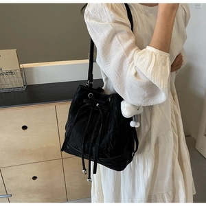 Detail of black drawstring bucket bag with texture and plush doll charm on a model