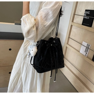 Detail of black drawstring bucket bag with a white cloud plush charm and pleated texture