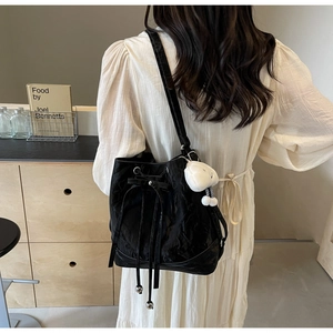 Detail of black bucket bag with pleated texture and a cute white cartoon keychain charm
