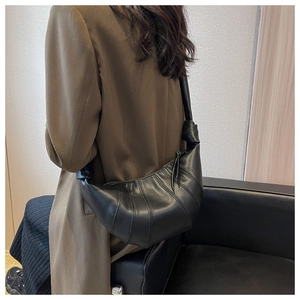 Detailed view of black croissant bag with knotted shoulder strap on a model