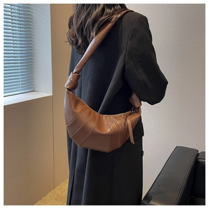 Detail of a brown pleated crescent bag with stylish knotted shoulder strap on a model