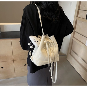 Detail view of cream drawstring bucket bag with bow tie and fluffy cloud charm accessory