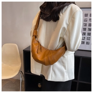 Detailed view of the caramel leather croissant bag worn over the shoulder in a minimal setting
