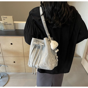 Close-up of light grey pleated bucket bag with drawstring closure and plush pendant