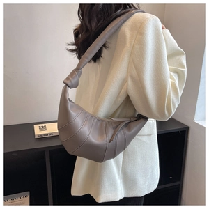 Detail of taupe crescent croissant bag with pleated design and knotted strap on model