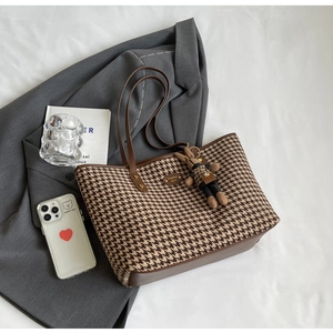 Detail view of houndstooth tote bag with leather straps and a decorative rabbit pendant