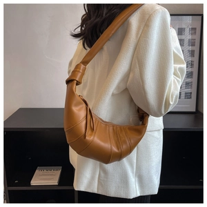 Close-up of caramel leather croissant bag with knotted strap detail and pleated seams