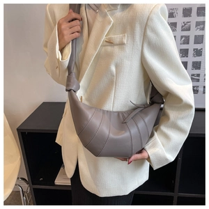Detail of grey croissant bag showing pleated stitching and large knot on shoulder strap