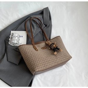 Detail of houndstooth tote bag with brown leather handles and a cute doll charm