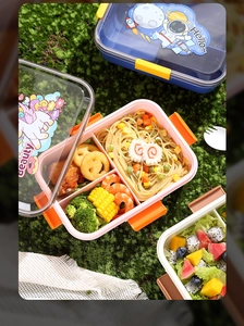 Top view of divided lunch boxes with pasta and fruit on green moss and white cloth