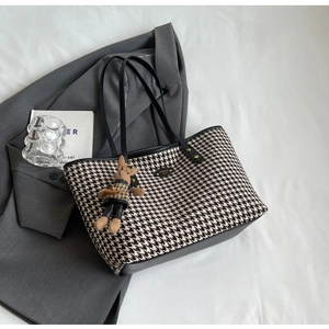Close-up of houndstooth tote bag with leather handles and a cute plush rabbit charm