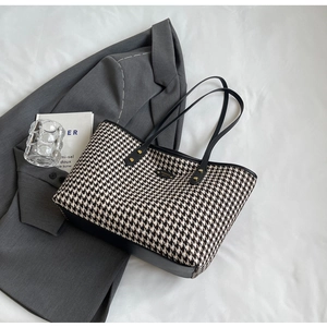 Close-up of houndstooth tote bag detail with brand metal logo and black leather straps