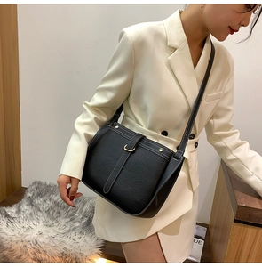 Detail of black pebbled leather crossbody bag with white stitching and gold hardware buckle
