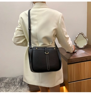 Detail of black pebbled leather saddle bag with white contrast stitching and gold metal buckle