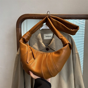 Caramel brown croissant crossbody bag with signature curved stitching and knotted strap