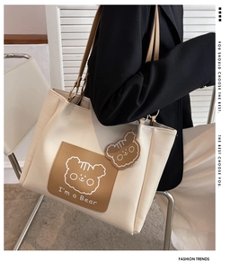 Detail of bear patch and hanging bear charm on a cream white leather tote bag