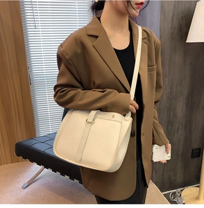 Detail of cream pebbled leather crossbody bag featuring gold hardware on a model jacket