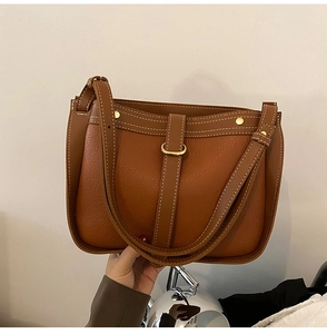 Detail of brown lychee leather shoulder bag with white contrast stitching and gold buckle