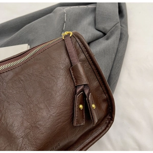 Dettaglio macro della borsa in pelle marrone scuro con cerniera e nappa dorata borchiata