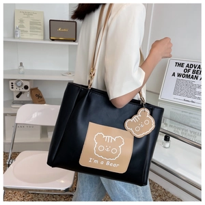 Detail of a black leather tote bag with a cartoon bear pocket shown on a model's shoulder