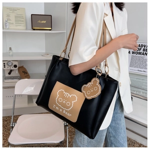 Detailed view of black tote bag featuring a cartoon bear patch and matching leather charm