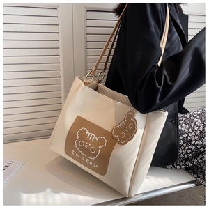 Detail of white tote bag featuring brown cartoon bear patch and matching leather strap