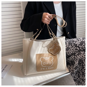 Detail of creamy white tote bag with cute cartoon bear patch and soft leather texture
