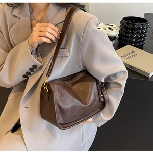 Borsa Boston in pelle marrone scuro con finiture dorate indossata come borsa a spalla
