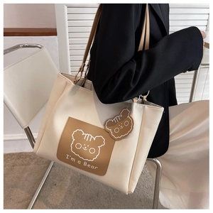 Detail of minimalist cream tote bag with bear print and brown charm shown on a model