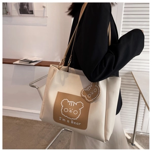 Detail of off-white faux leather tote bag with brown bear embroidery and matching charm