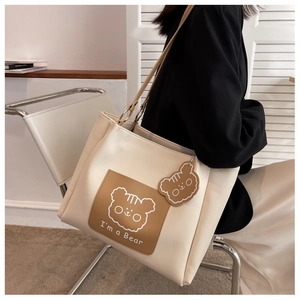 Detail of cream tote bag with bear graphic and matching bear pendant in casual setting