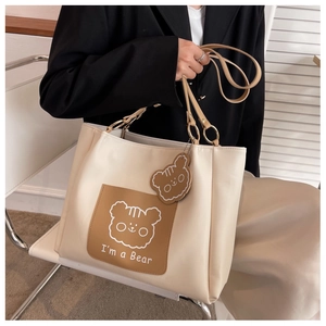 Detail of cream tote bag with cartoon bear print and matching charm held by a model