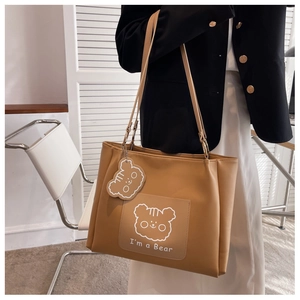 Detail of camel leather tote bag with cute bear charm and pocket carried by a model