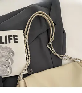 Detail of a creamy beige shoulder bag with metal chain strap and flap closure
