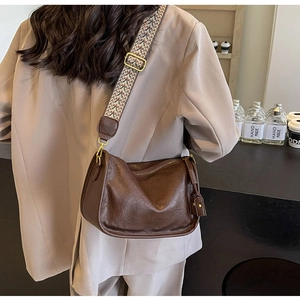 Borsa a cilindro in pelle marrone scuro con un'ampia tracolla intrecciata in stile etnico