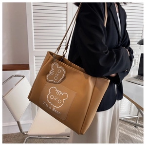 Detail of khaki tote bag with bear graphic and bear charm shown in office setting