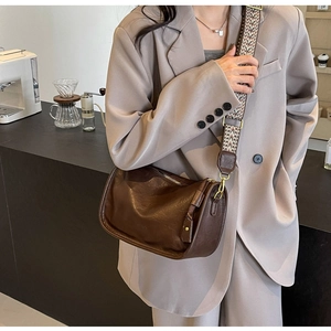 Dettaglio borsa a bauletto in pelle marrone con ampia tracolla in tessuto colorato