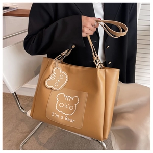 Detail of light tan leather tote bag with cartoon bear print and bear-shaped charm