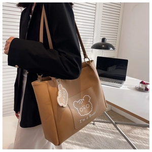 Detail of khaki tote bag featuring cartoon bear print and a cute bear charm accessory