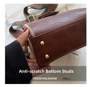 Detail der braunen Lederhandtasche mit schützenden goldenen Metallfüßen und feinen Nähten