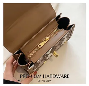 Close-up of golden metal zipper and brown plaid texture on a minimalist crossbody bag