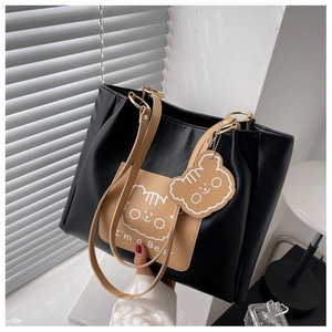 Close-up of black leather tote bag with cartoon bear graphic and matching plush charm