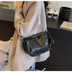 Vista laterale della borsa a tracolla nera a pieghe con dettagli dorati e blazer beige