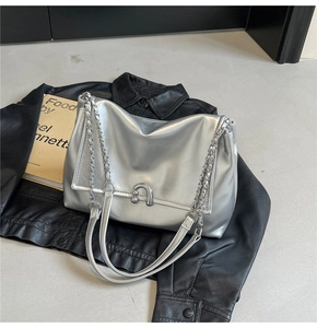 Close-up of a metallic silver shoulder bag with a designer U-shaped buckle on black leather