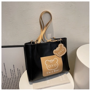 Close-up of black tote bag featuring a brown bear pocket and matching cute charm