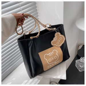 Detail of black tote bag with cartoon bear print, khaki straps and matching bear charm