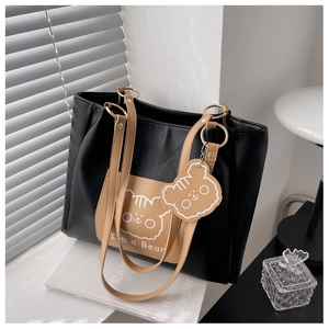 Detail of black and camel tote bag featuring cartoon bear pocket and matching charm